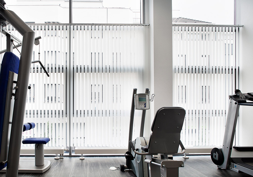 Fensterfront in Fitnessstudio in halber Hoehe mit Lamellenvorhang verschattet