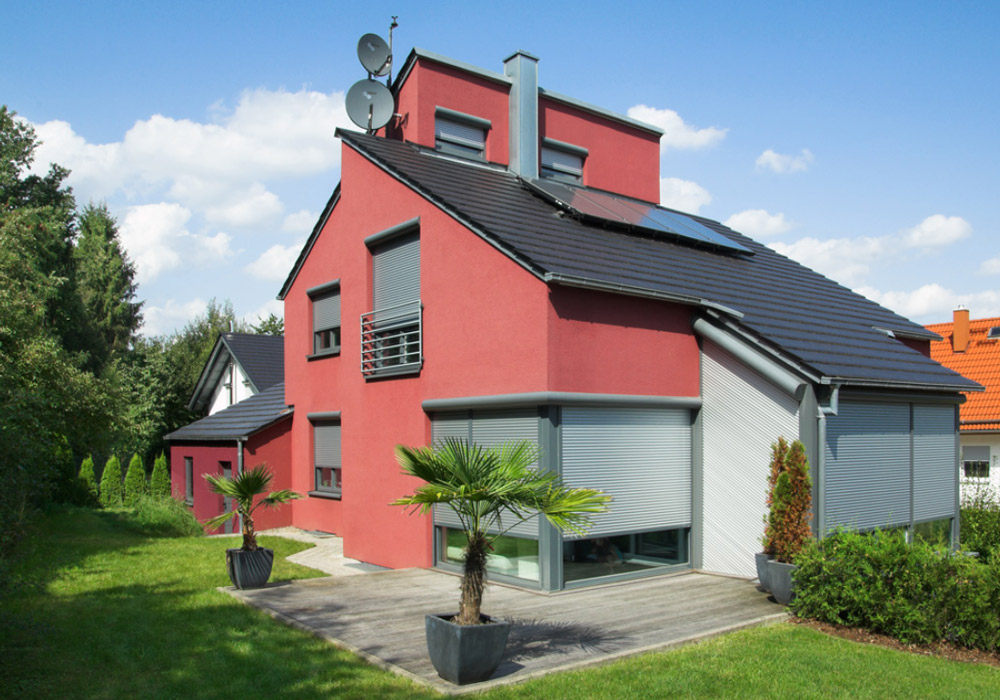 Rotes verwinkeltes Haus mit heller Terrassenfensterbeschattung mit Rollläden
